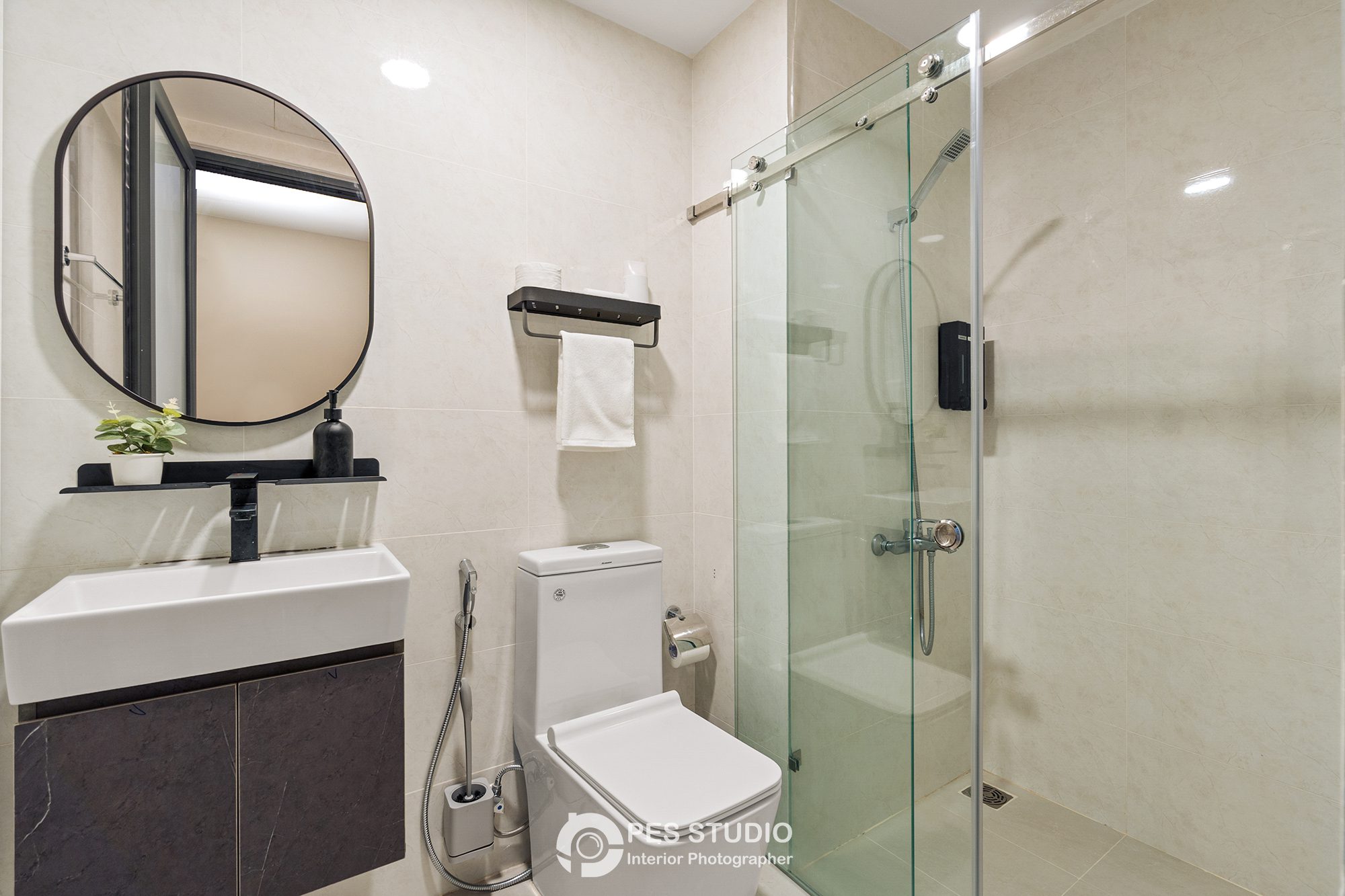 Phòng tắm căn hộ Soho Residence với gương tròn viền đen và buồng sen kính