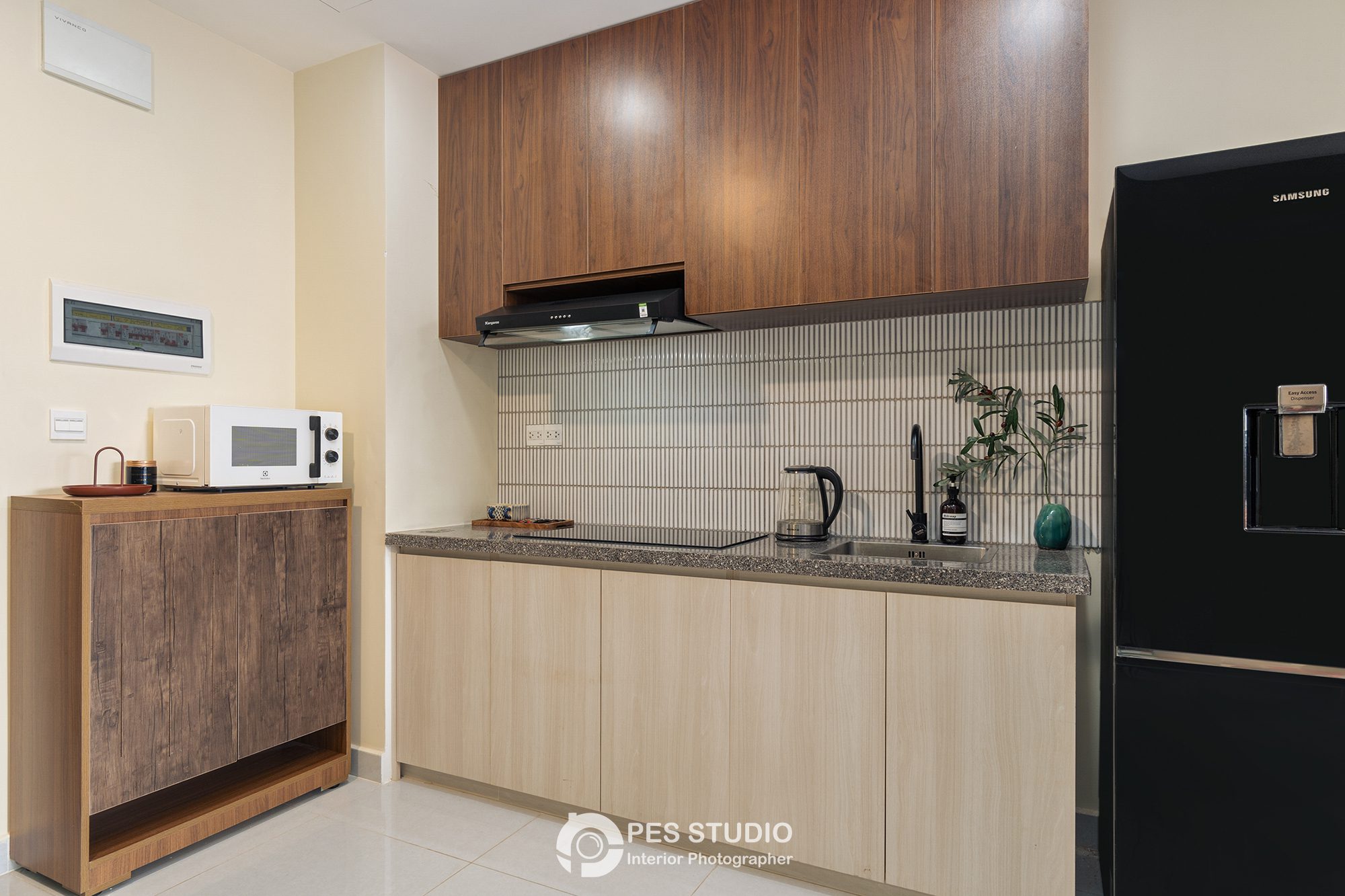 Bếp căn hộ Soho Residence với tủ gỗ sáng, tủ lạnh đen và mặt bếp đá