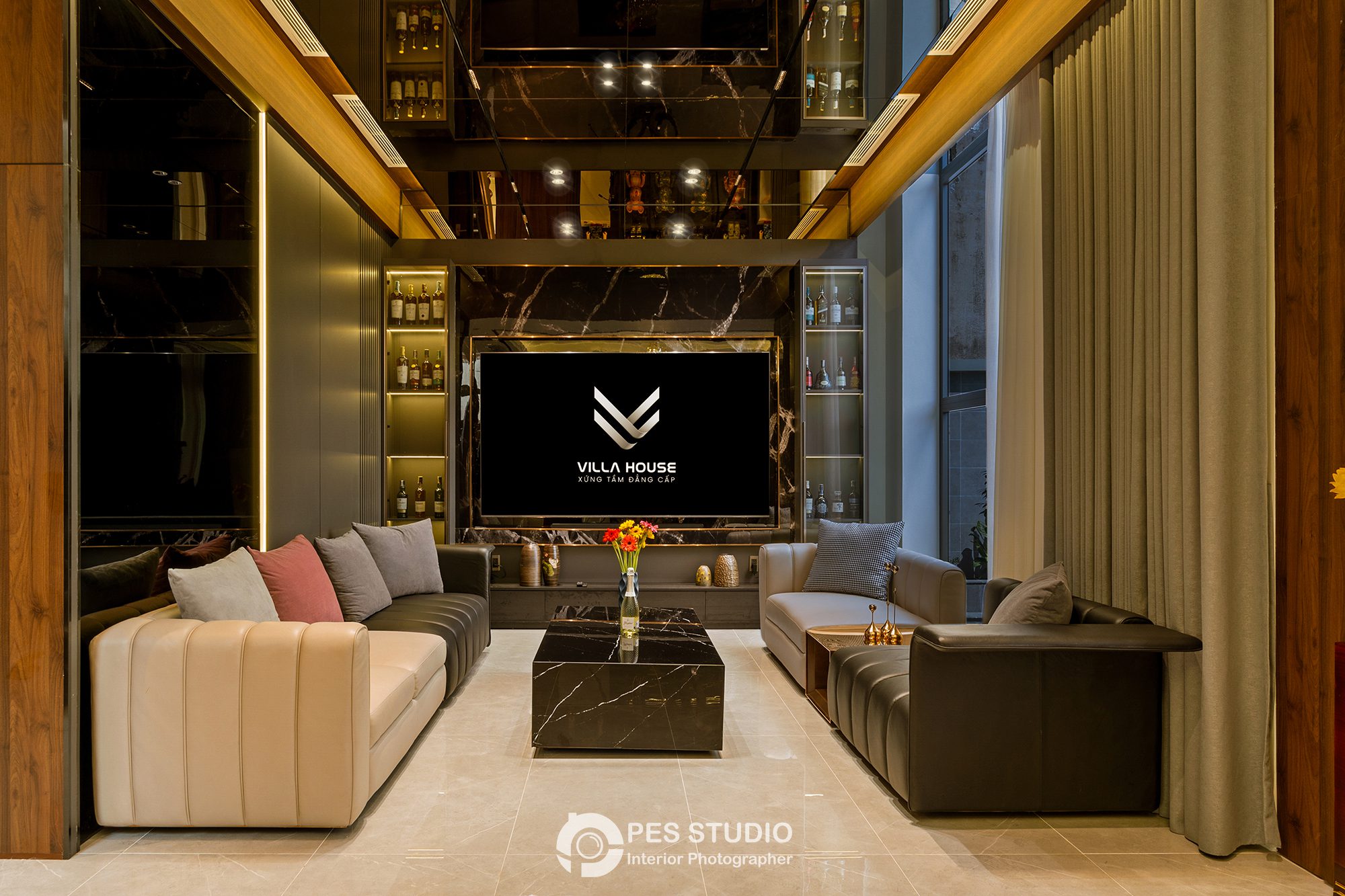 Phòng khách biệt thự với sofa xám, tủ rượu kính và trần thông tầng
