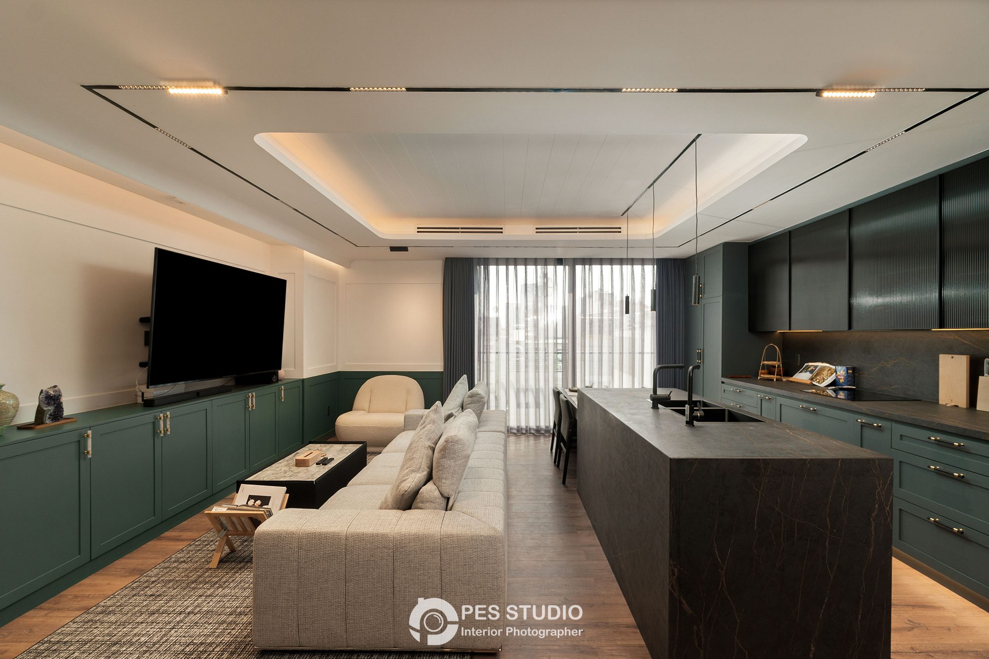 Phòng khách liền bếp căn hộ Ahouse với sofa sáng màu, TV treo tường và đảo bếp đá đen
