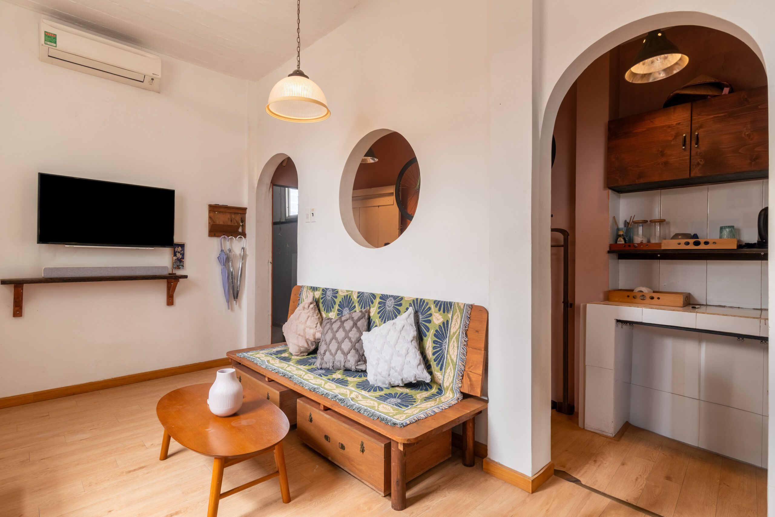 Phòng khách homestay 42 Nguyễn Huệ với TV, gương tròn và bếp phía sau