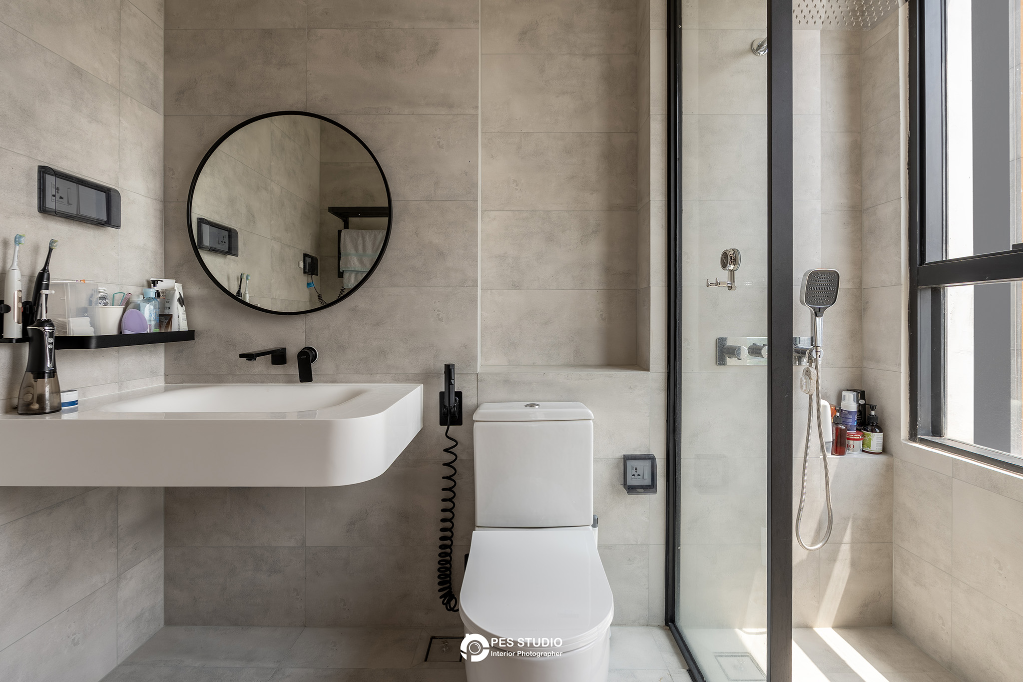 Phòng tắm với gương tròn, lavabo treo và bồn cầu trong căn hộ
