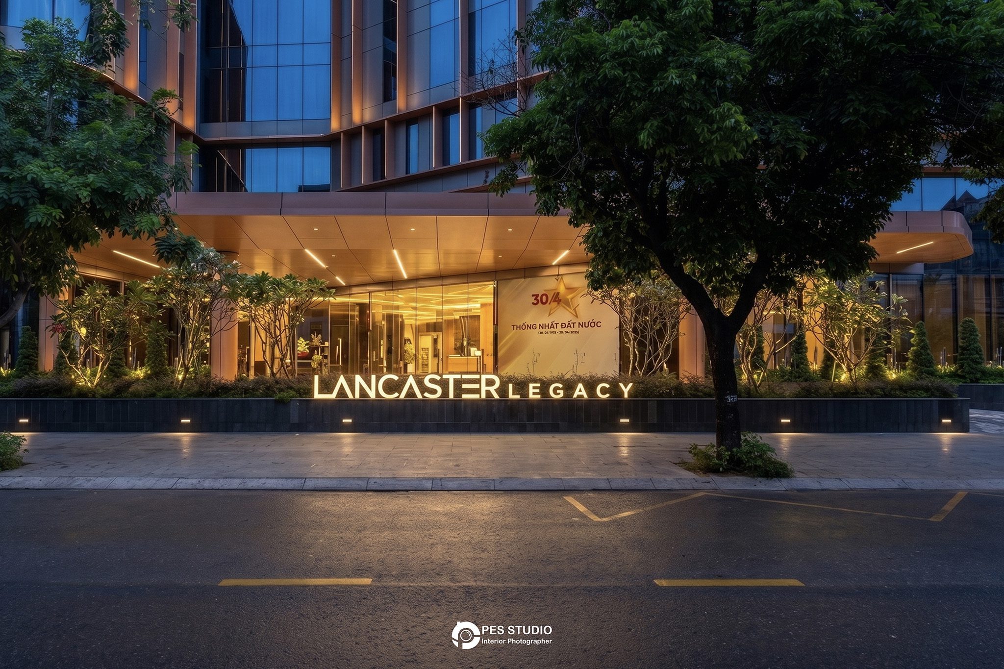Cổng vào Lancaster Legacy Tower với biển hiệu và hàng cây