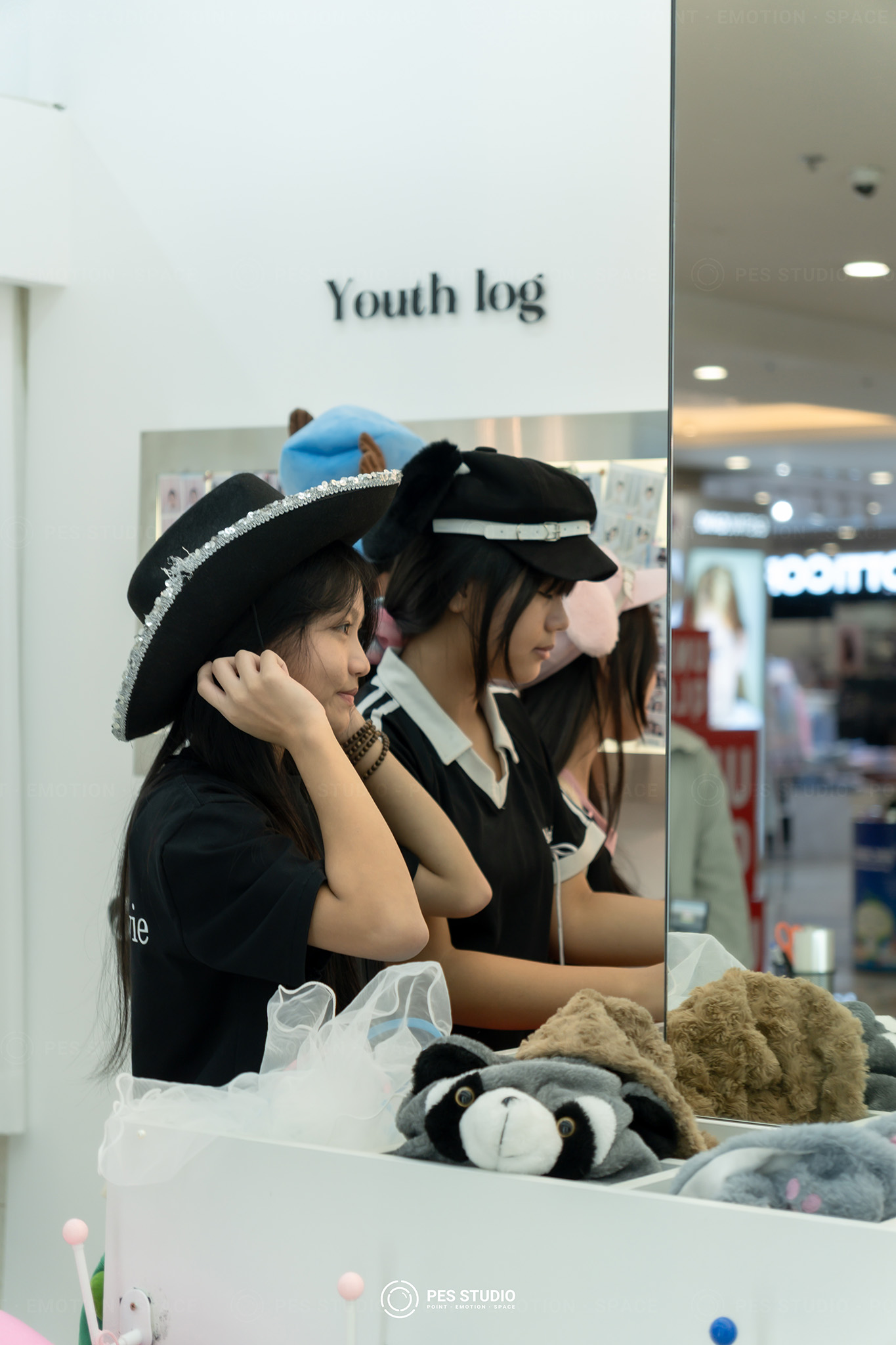 Ba khách nữ thử mũ trước gương trong cửa hàng Youth Log