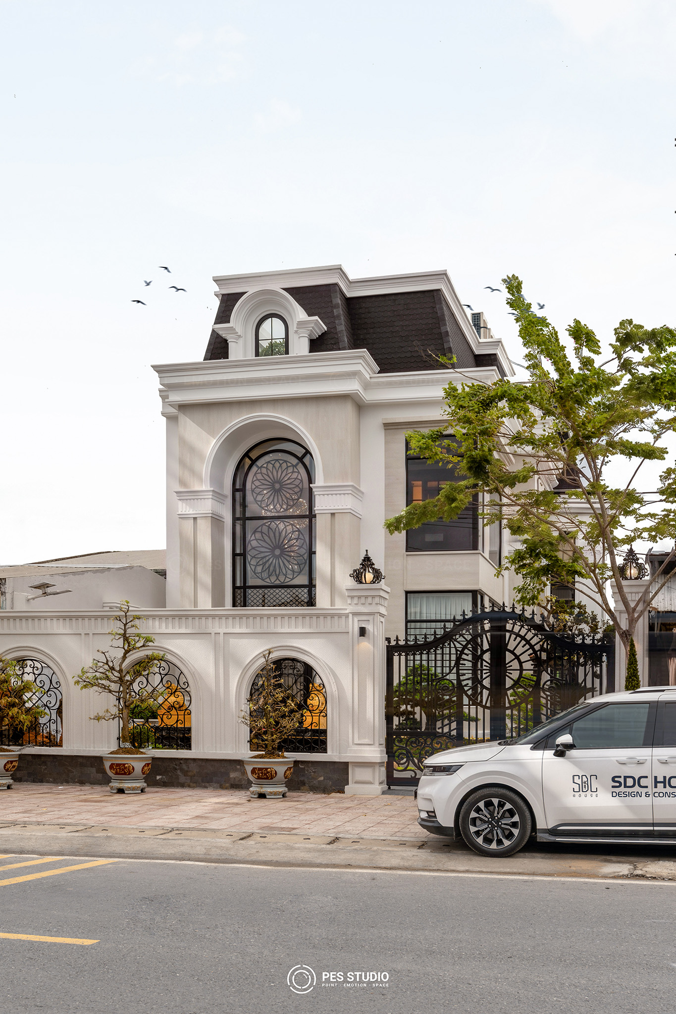 Cửa vòm cao hai tầng với hoa sắt uốn hình bông cúc trên mặt tiền villa tân cổ điển
