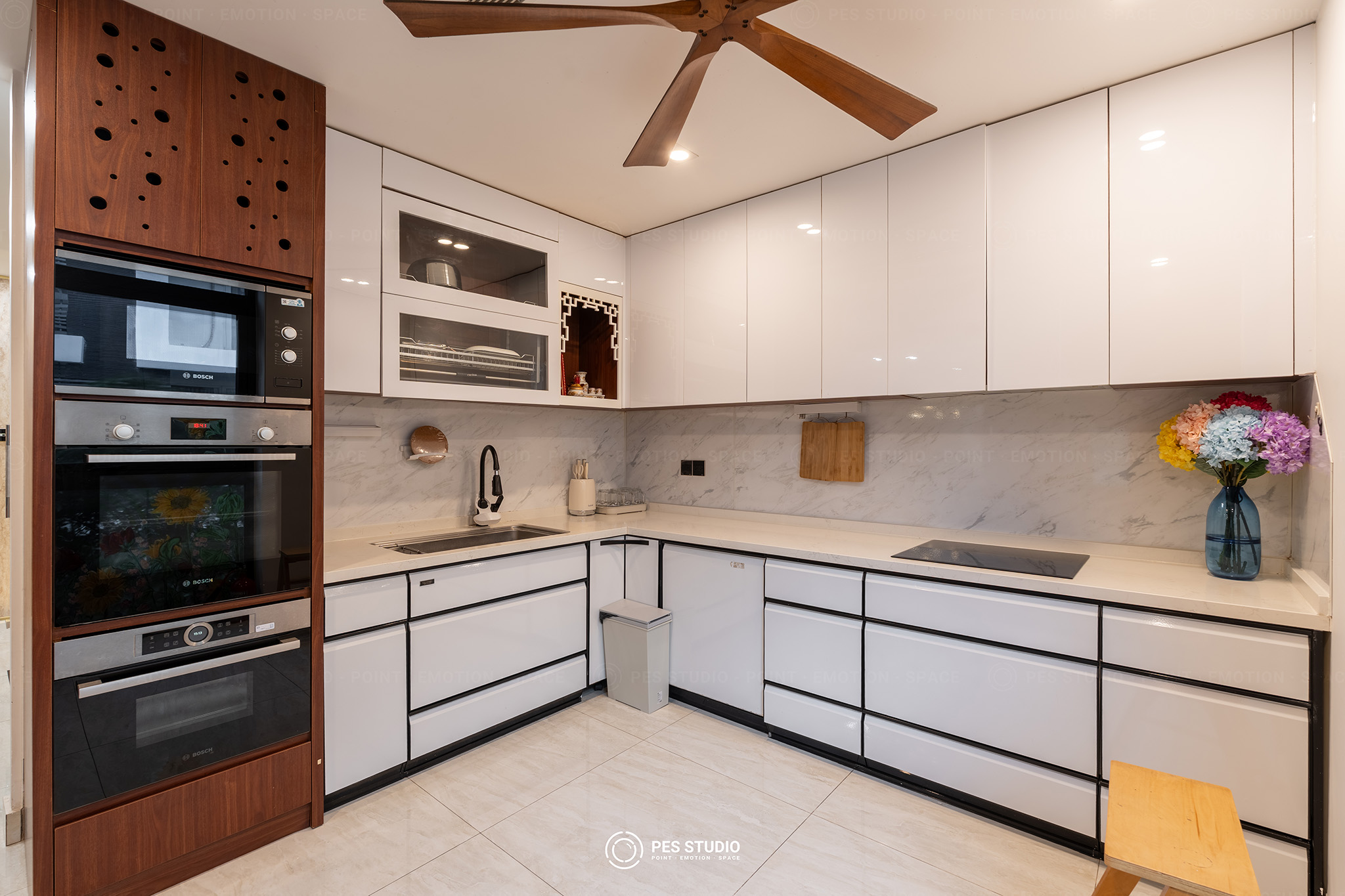 Bếp trắng chữ L trong villa quận 7 với lò âm tường và quạt trần cánh gỗ