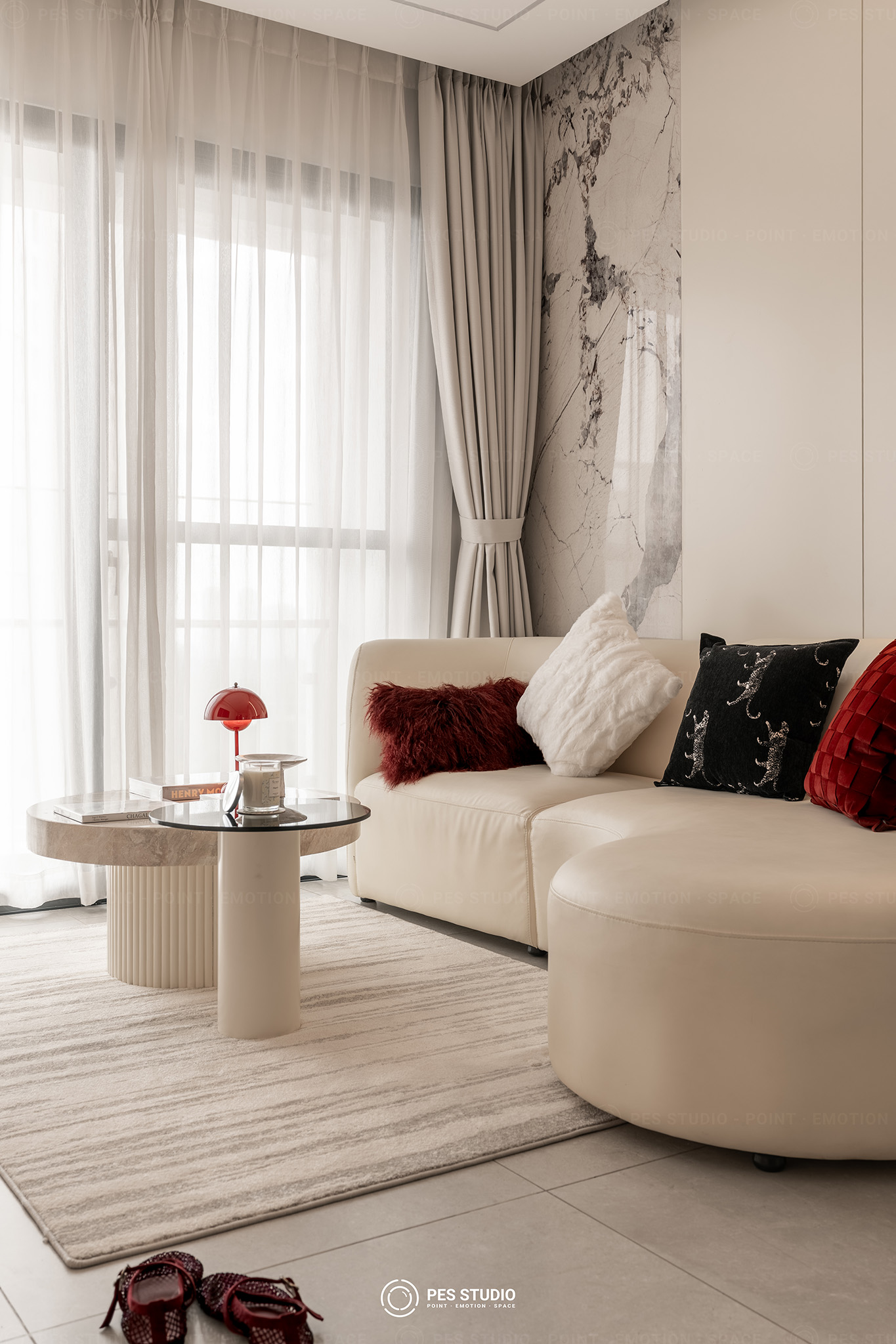 Sofa cong bọc vải kem với gối đỏ đô và bàn trà tròn mặt đá trong căn hộ Antonia