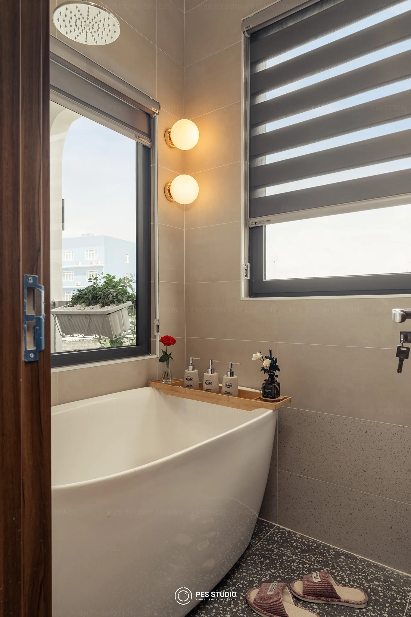 Bồn tắm góc với đèn cầu đôi và sàn terrazzo tại phòng tắm Cô Hai Homestay Mỹ Tho