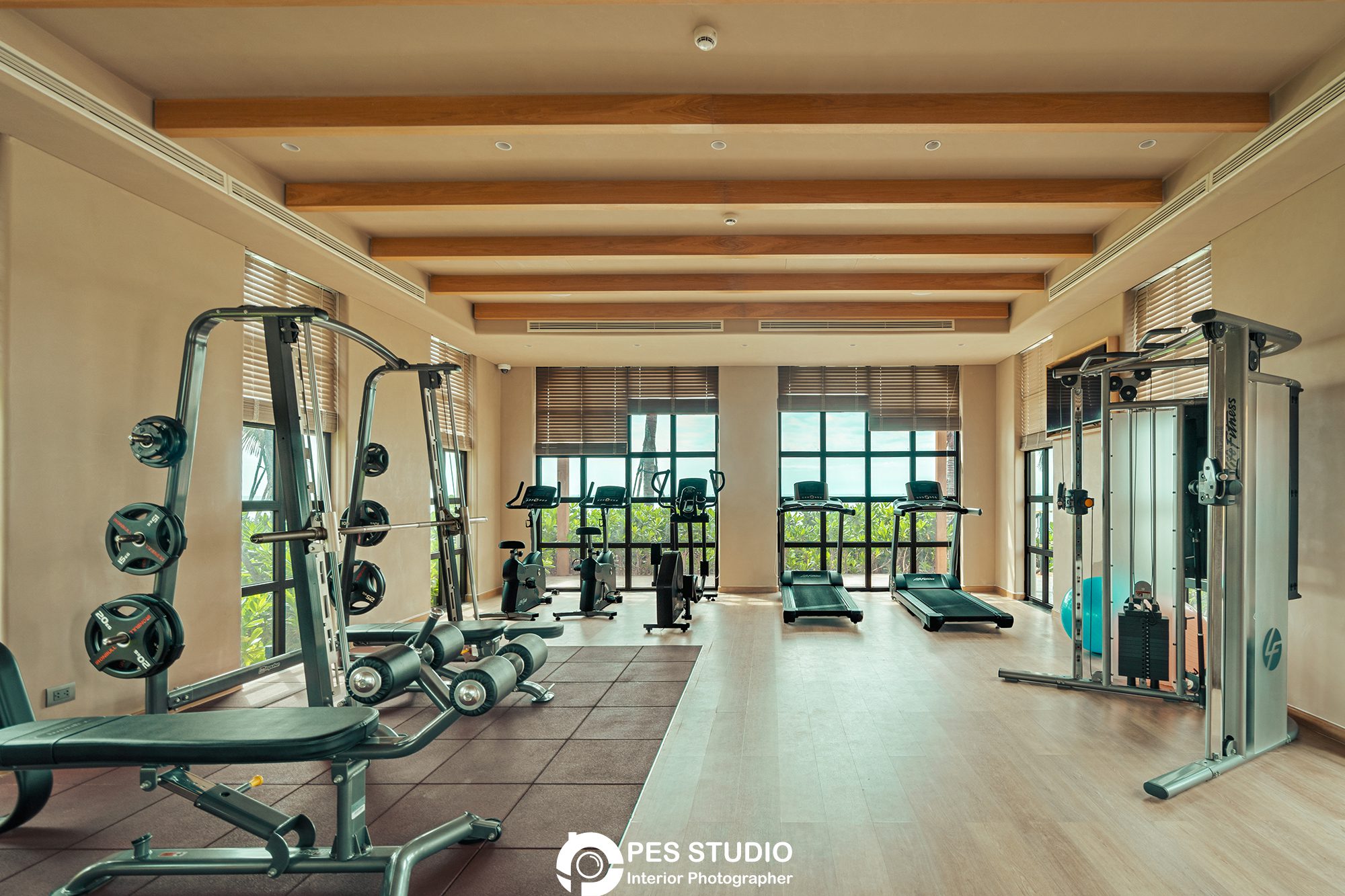 Chụp Ảnh Nội Thất Phòng Gym 1 Chụp ảnh nội thất phòng gym resort với trần gỗ và dãy thiết bị dọc tường kính